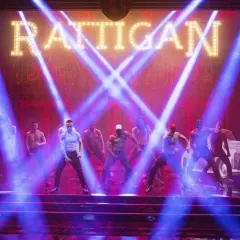 Mężczyźni tańczą na scenie w świetle niebieskich reflektorów, pod neonowym napisem "RATTIGAN". To scena z filmu Magic Mike 1.