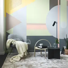 En bekväm fåtölj med pläd framför en vägg där man valt att måla mönster i geometriska former.