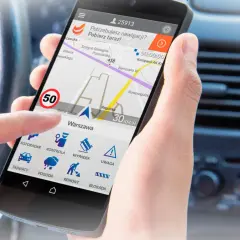 Aplikacja nawigacyjna na telefonie pokazuje mapę z trasą i ikoną fotoradaru. Kierowca w Niemczech korzysta z niej, by uniknąć mandatów.