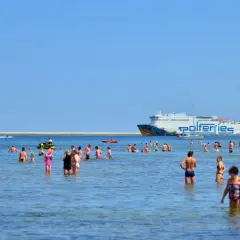 Ludzie kąpią się w morzu, a w tle widać prom Polferries. Szukasz informacji o prom Świnoujście-Ystad cena?