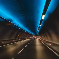 Jadące samochody w tunelu drogowym z niebieskim oświetleniem sufitowym.
