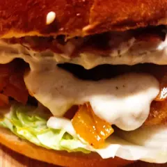 Zbliżenie na soczystego kotleta do burgera z serem, warzywami i sosem.