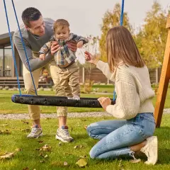 Rodzina cieszy się wspólnymi zabawami na podwórku. Tata trzyma dziecko na huśtawce, a mama zachęca do zabawy.