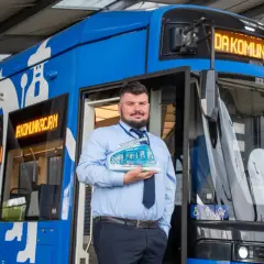 Pracownik MPK trzymający model tramwaju przed niebieskim pojazdem. To symbol publiczny transport krakow.