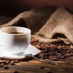 Aromatic coffee beans surround a white cup. Zastanawiasz się, ile kofeiny ma kawa w 100 ml?