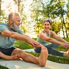 Couple souriant pratiquant le qi gong en plein air, étirant leurs jambes sur des tapis de yoga dans un parc ensoleillé.