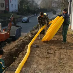 Arbeiter verlegen gelbe Rohre für die Drainage am Keller. Ein Bagger steht bereit.