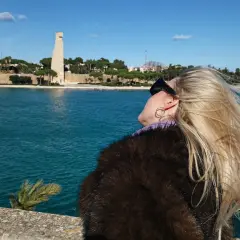 Widok na pomnik i morze w Brindisi. Wiatr rozwiewa blond włosy kobiety w futrze.