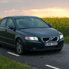 Ciemnozielone Volvo S40 2.0 diesel jedzie wiejską drogą wśród kwitnącego rzepaku o zachodzie słońca.