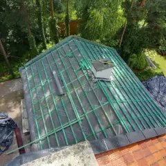 Trwa remont dachu. Widoczna konstrukcja więźby, folia dachowa i kominek. Zgłoszenie prac budowlanych.