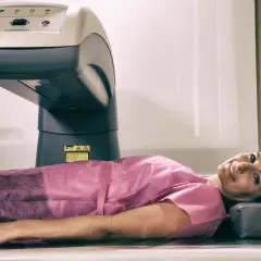 Kobieta leży pod aparatem do badania densytometrycznego. Uśmiecha się, czując się komfortowo podczas procedury.