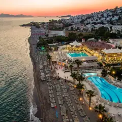 Widok z lotu ptaka na Armonia Holiday Village o zachodzie słońca. Widoczne baseny, plaża z leżakami i budynki hotelowe.