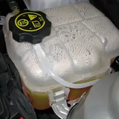 Depósito de expansión del coche con agua y burbujas. El tapón negro tiene símbolos de advertencia.