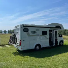 Kamper na trawie, gotowy na przygodę. Idealne miejsce na pola namiotowe Mazury, z widokiem na jezioro i las.