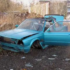 Turkusowy, zniszczony samochód na złomowisku. Drzwi i maska otwarte, jakby ktoś właśnie zaczął zastanawiać się, jak zezłomować auto.