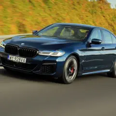 Ciemnoniebieskie BMW 545e pędzi autostradą, otoczone zielenią.