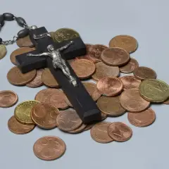 Holzkreuz mit Korpus, Rosenkranz und Münzen. Ein Symbol für das Kirchgeld in Bayern.