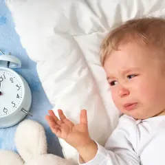 Płacz 1,5 rocznego dziecka, które nie chce spać. Obok budzik i pluszaki.