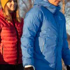 Två personer i vinterkläder, en i röd och en i blå, varmaste dunjackan, står utomhus i snö.