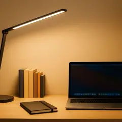 Escritorio con portátil, libros y flexos modernos iluminando la escena.