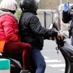 Agente de policía detiene a pareja en moto. Podrían recibir una multa por ir sin casco.