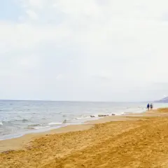 Spokojne morze i piaszczysta plaża na Zakynthos w maju. Kilka osób spaceruje brzegiem, ciesząc się łagodnym słońcem i ciszą.