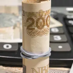 Zrolowany banknot 200 zł na kalkulatorze, obok inne nominały. Analiza millenium kurs akcji.