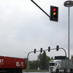 Na skrzyżowaniu widać czerwone i żółte światła. Białe kamery nad światłami monitorują ruch.