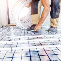 Worker installing underfloor heating pipes on a grid system.