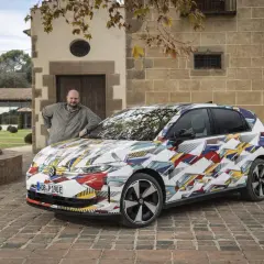 Man lutar sig mot en Volkswagen ID.2 med ett färgglatt, geometriskt mönster.