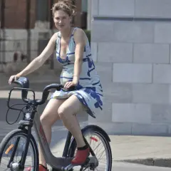 Uśmiechnięta ciężarna kobieta w letniej sukience jeździ na rowerze miejskim, pokazując, że **czy w ciąży można jeździć na rowerze** jest możliwe.