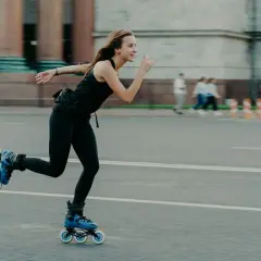 Dziewczyna na rolkach w czarnym stroju, z wiatrem we włosach, tworzy dynamiczne rolki efekty na miejskim asfalcie.