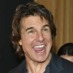 Uśmiechnięty Tom Cruise, którego twarz przypomina scenę z filmu o sekcie, z szeroko otwartymi ustami i widocznymi zębami.