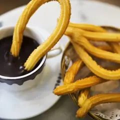 Churros sin gluten dorados y crujientes, uno sumergido en una taza de chocolate caliente espeso.