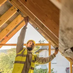 Operaio con livella controlla la pendenza del tetto, un passo fondamentale per le **idee per rinnovare casa** e creare nuovi spazi abitativi.