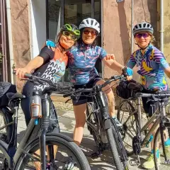Three friends ready for guided bike tours in Europe, smiling with their bikes in front of a charming shop.