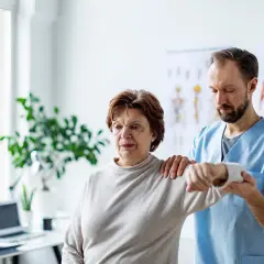 Physiotherapeut hilft einer Frau mit einer schmerzenden, verklemmten Schulter bei der Bewegung.
