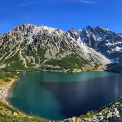 Piękne Tatry dla początkujących: Morskie Oko otoczone zielenią i ośnieżonymi szczytami. Tłumy turystów podziwiają widok.
