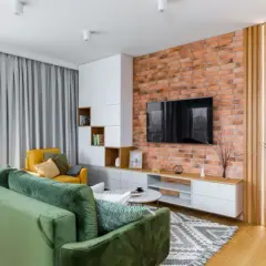 Nowoczesny salon z zieloną kanapą, żółtym fotelem, ceglaną ścianą i pionowymi lamelami.
