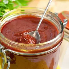 Domowy sos barbecue przepis. Słoik pełen pysznego, gęstego sosu, z łyżeczką do degustacji.