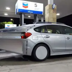 Silverbil med en stor, silverfärgad aerodynamisk förlängning bak. En uppfinning för att spara bensin vid en Chevron-mack.