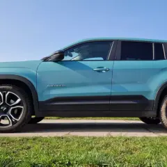 Turkusowy suv premium Jeep Avenger z czarnymi akcentami i felgami stoi na tle błękitnego nieba.