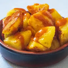Knusprige patatas bravas in einer Schale, mit einer würzigen Sauce übergossen. Ein Klassiker der spanischen Tapas-Kultur.