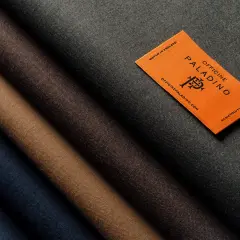 A selection of different types of wool fabric in shades of blue, brown, and grey, with an orange tag from Officine Paladino.