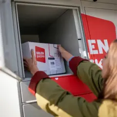 Kobieta wkłada paczkę z logo "Orlen paczka" do skrytki automatu paczkowego.