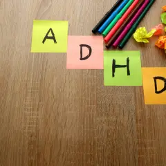 Kolorowe karteczki z literami A, D, H, D układają się w napis ADHD. Obok leżą flamastry i pomięte kartki.