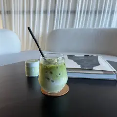 Un verre de lait matcha glacé, parfait pour profiter des bienfaits du matcha. Une petite boîte de matcha est à côté.