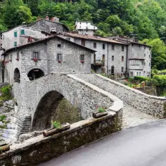 Ponte in pietra a Vergemoli, con case in pietra e vegetazione lussureggiante sullo sfondo. Le fabbriche di Vergemoli sembrano immerse nella natura.