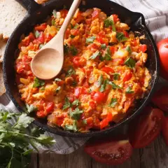 Pyszna jajecznica z pomidorami, podana w żeliwnej patelni, z chrupiącym pieczywem i świeżą natką pietruszki.