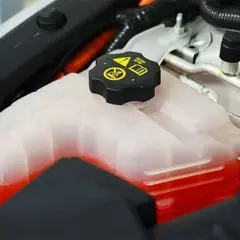 Depósito de refrigerante de coche con líquido rojo. La tapa negra tiene símbolos de advertencia. Se puede echar agua normal al coche si es necesario.